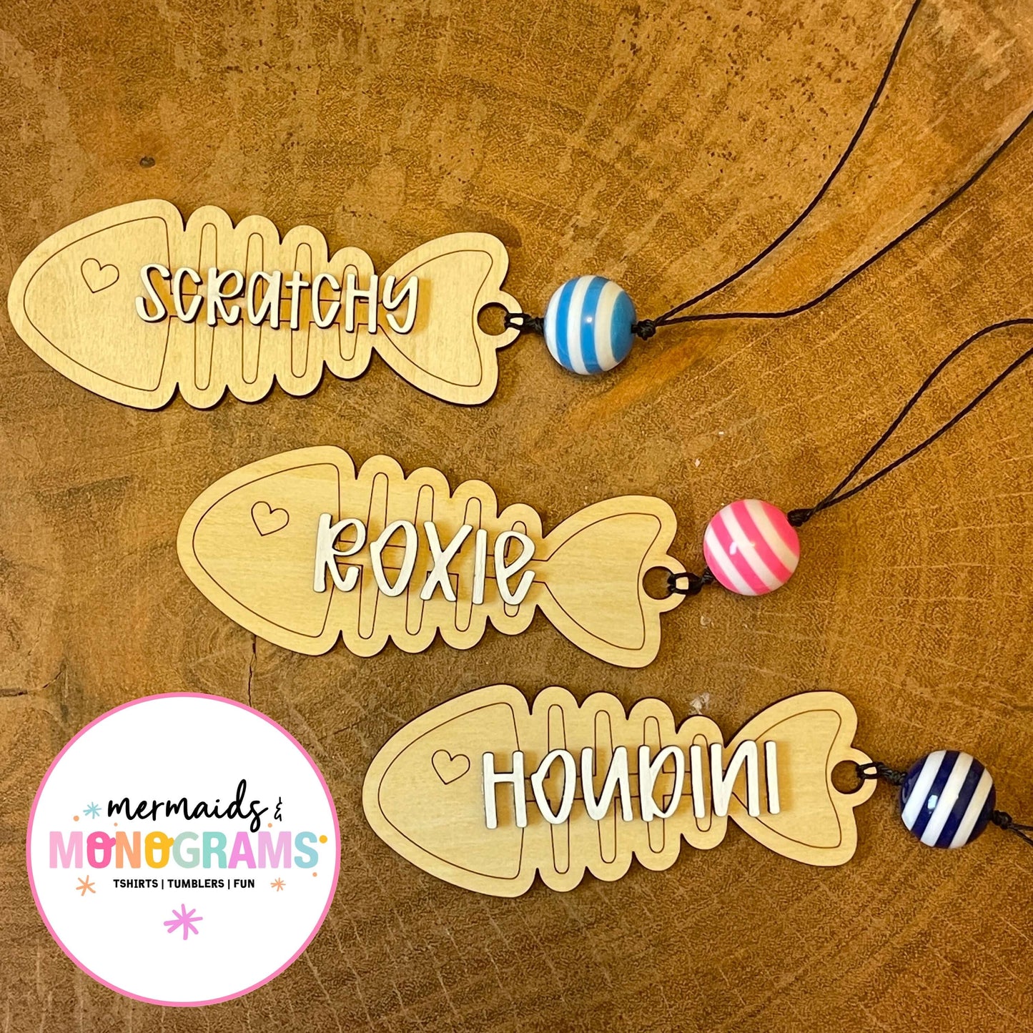 Three wooden fish-shaped name tags with colorful beads on a wooden surface