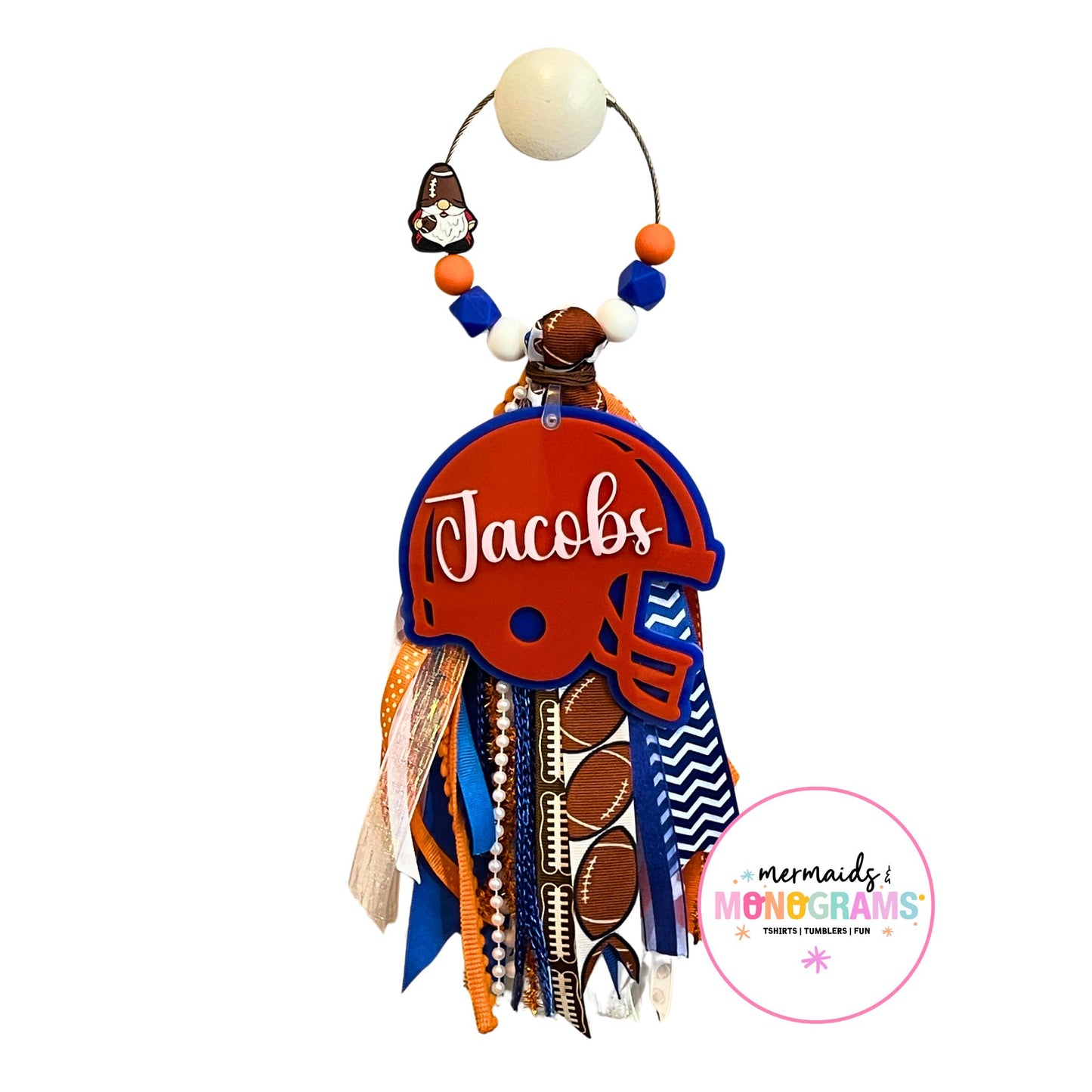 Custom football helmet bag tag with name โJacobsโ in white script on orange helmet, hanging with blue and orange ribbon tassel