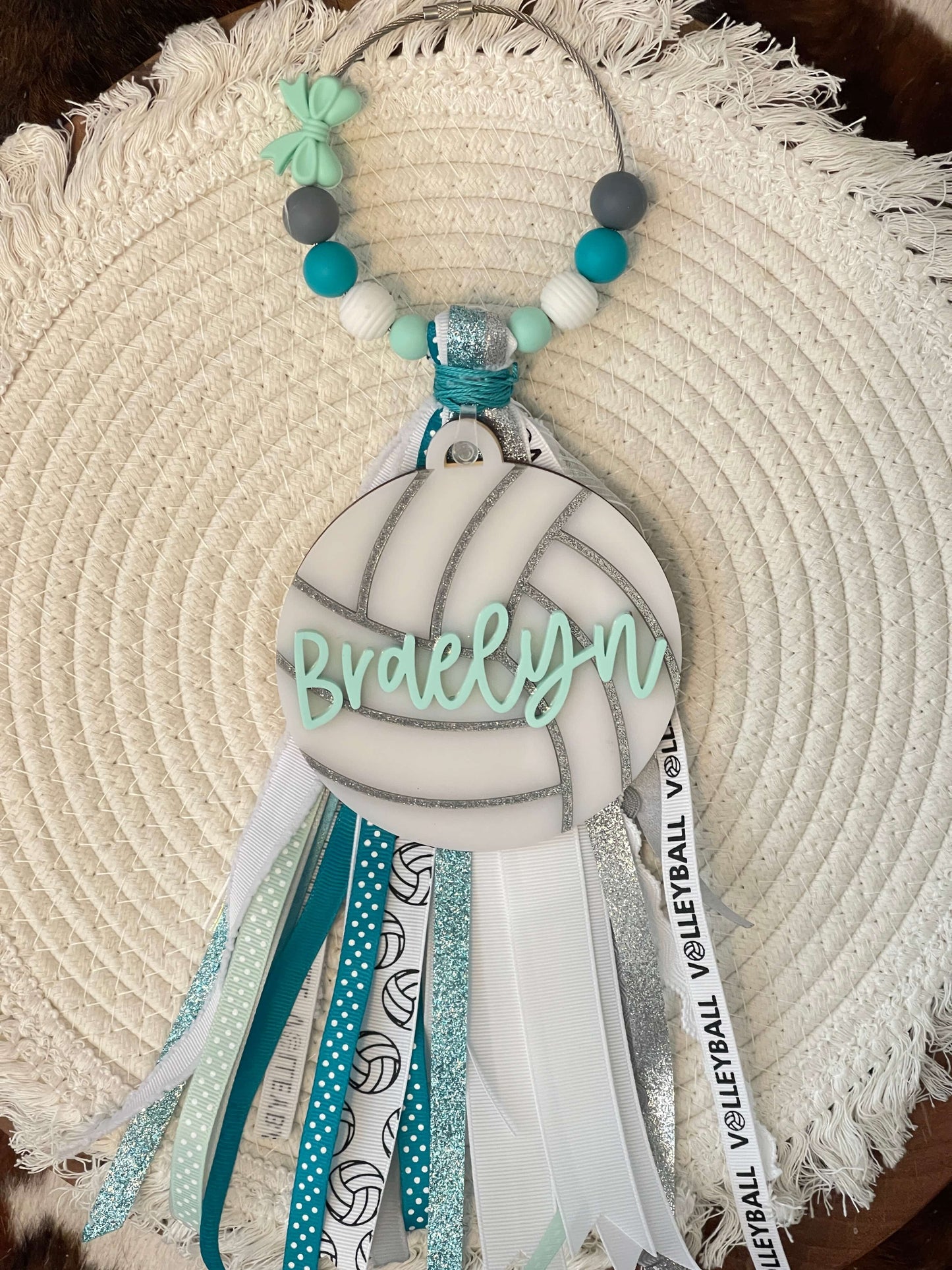 Decorative keychain with 'Braelyn' on a volleyball design, hanging on a textured surface.
