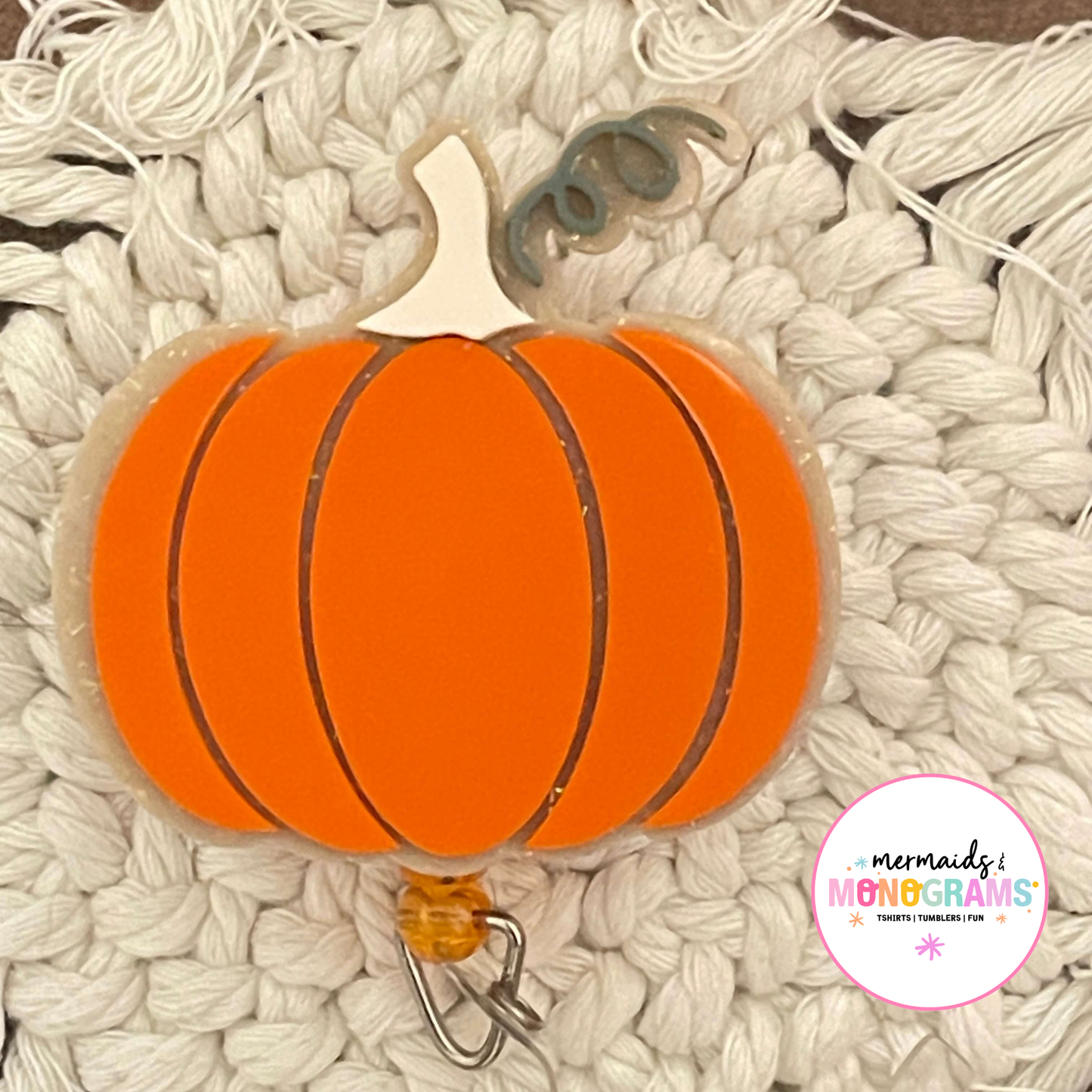 Close-up of acrylic pumpkin badge reel on textured white knit background