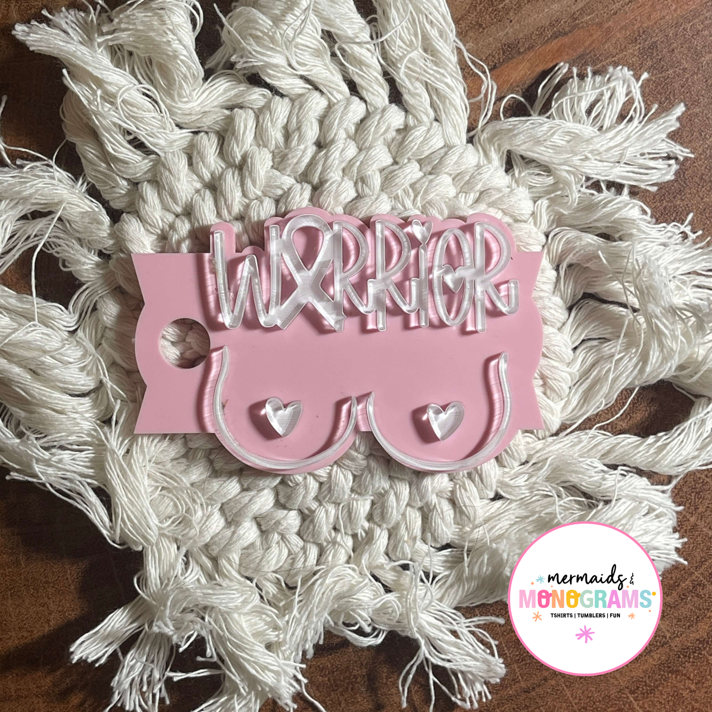 Flat lay of pink acrylic breast cancer “Warrior” topper styled on textured coaster