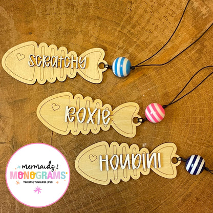Three wooden fish-shaped name tags with colorful beads on a wooden surface