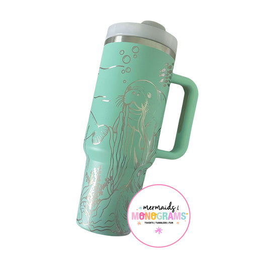 Seafoam green tumbler with silver laser-engraved manatee and coral illustrations