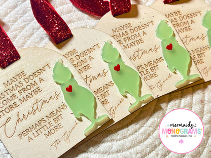 Close-up side angle of multiple handmade Grinch ornaments with red glitter ribbon, engraved holiday quote, and light green acrylic silhouette with a red heart accent.