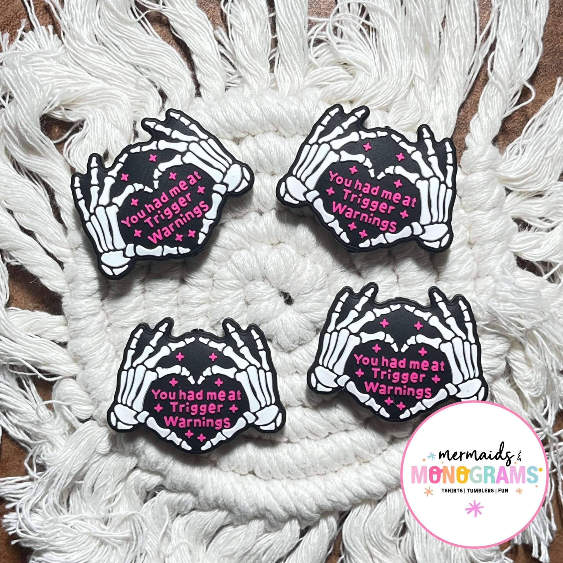 Four skeleton hand beads with text on a textured white surface, featuring the brand 'Mermaids & Monograms'.