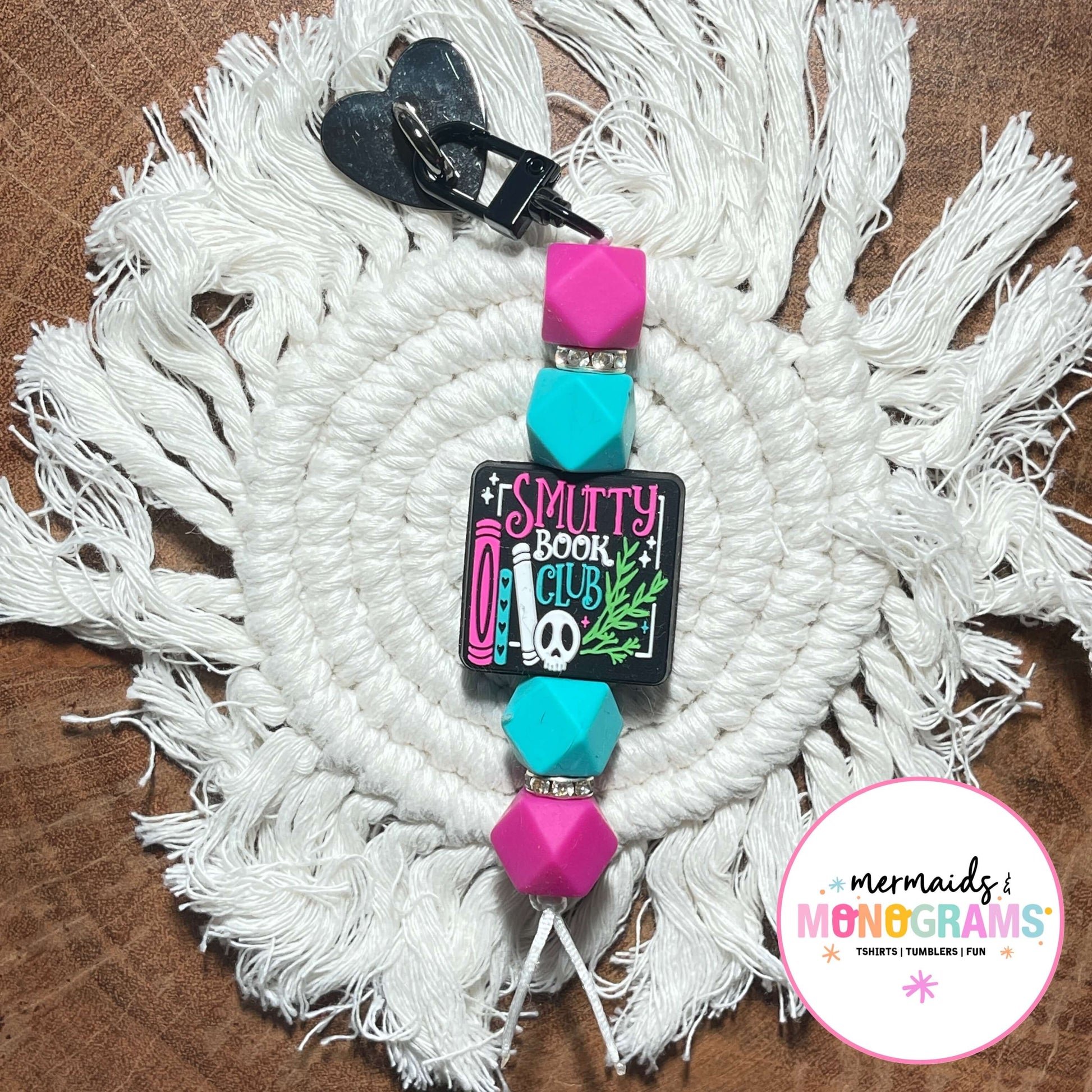 Keychain with colorful beads and 'Smutty Book Club' design on a white macramé wall hanging.