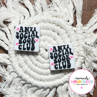 Two 'Anti Social Book Club' beads on a macrame surface with a brand logo in the corner.