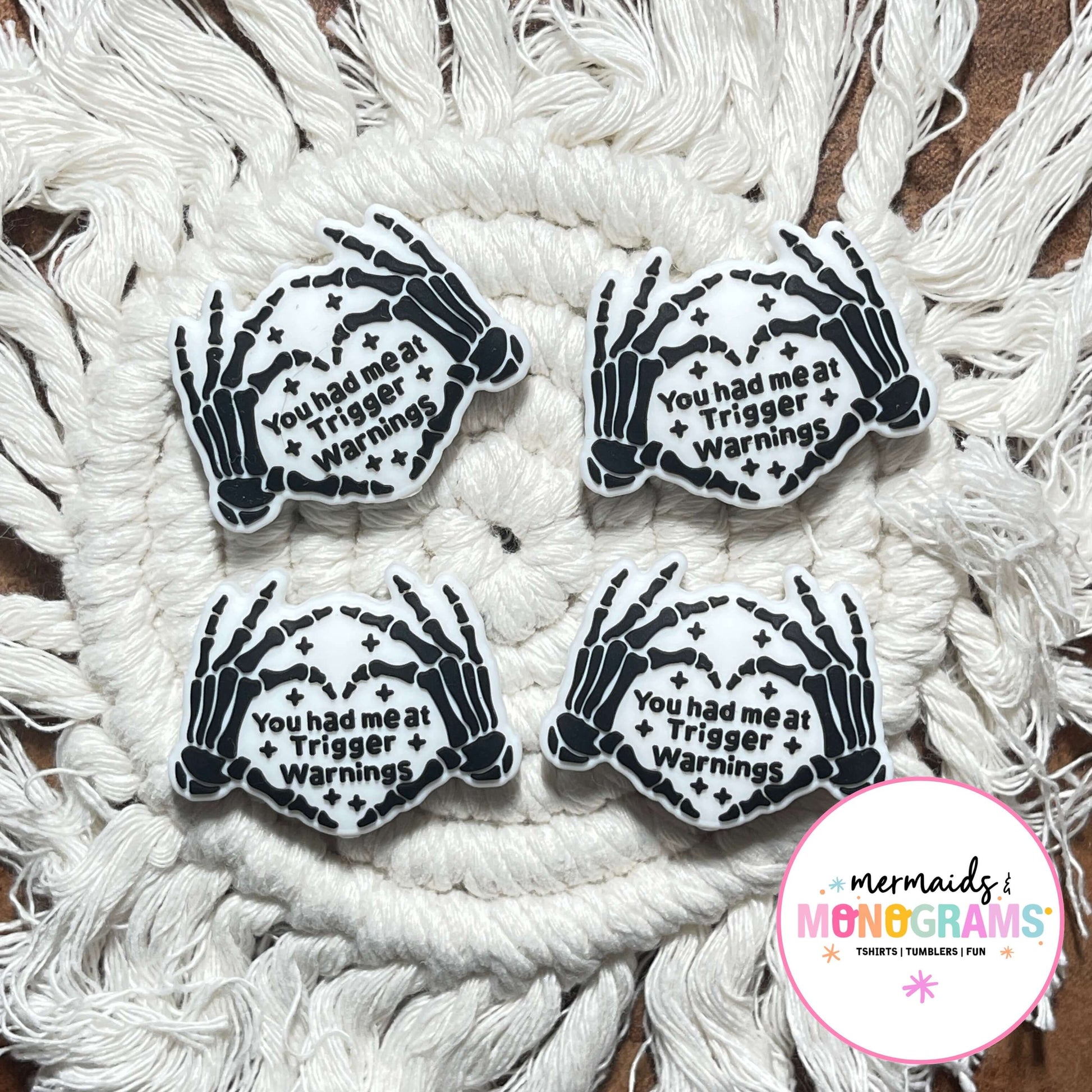 Four skeleton hand beads with text on a textured white surface, featuring the brand 'Mermaids & Monograms'.