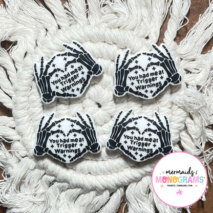 Four skeleton hand beads with text on a textured white surface, featuring the brand 'Mermaids & Monograms'.
