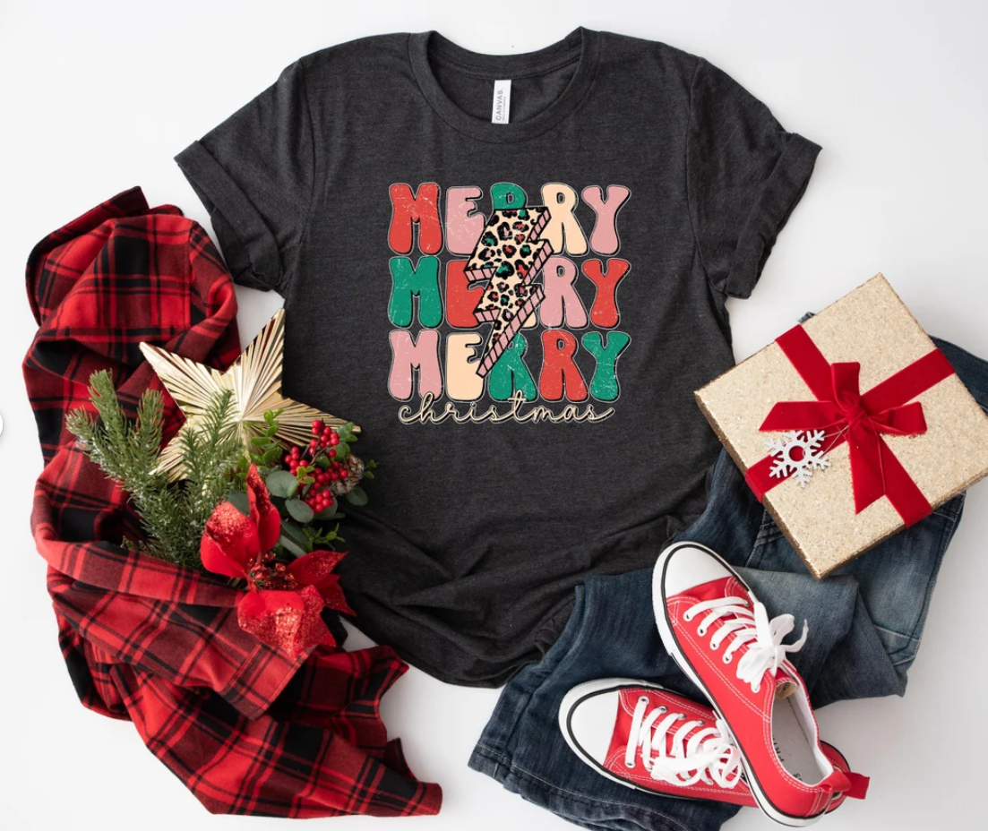 Black t-shirt with colorful 'Merry Christmas' design, red sneakers, plaid fabric, and gift box on a white background