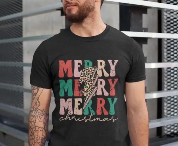 Man wearing a black graphic Christmas t-shirt with bold "Merry Merry Merry Christmas" text and a leopard print lightning bolt design, perfect for a trendy holiday outfit.