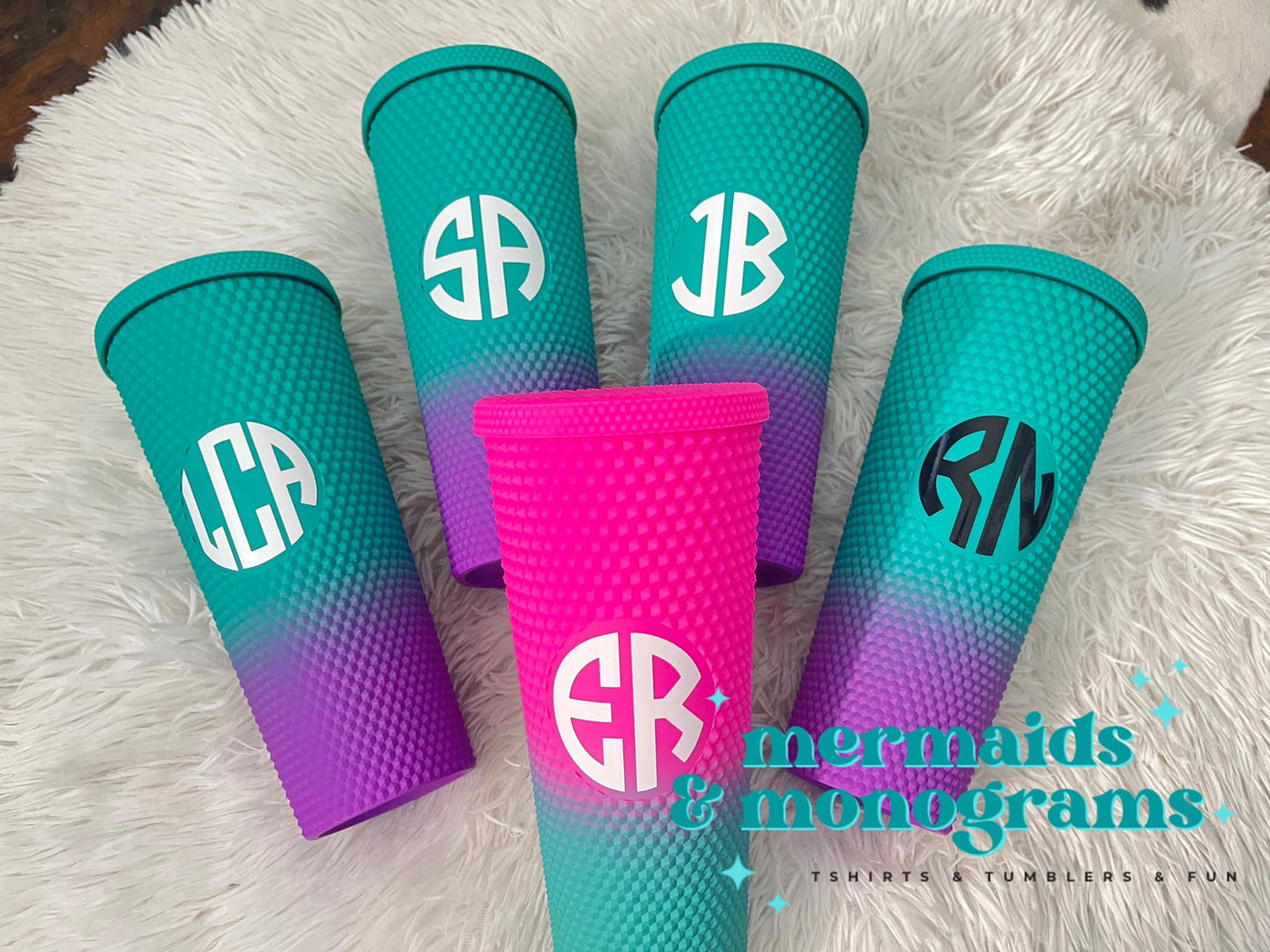 Group of colorful ombré studded tumblers with bold white monogram initials displayed on fuzzy rug