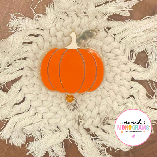 Flat-lay of pumpkin acrylic badge reel centered on white fringe macrame
