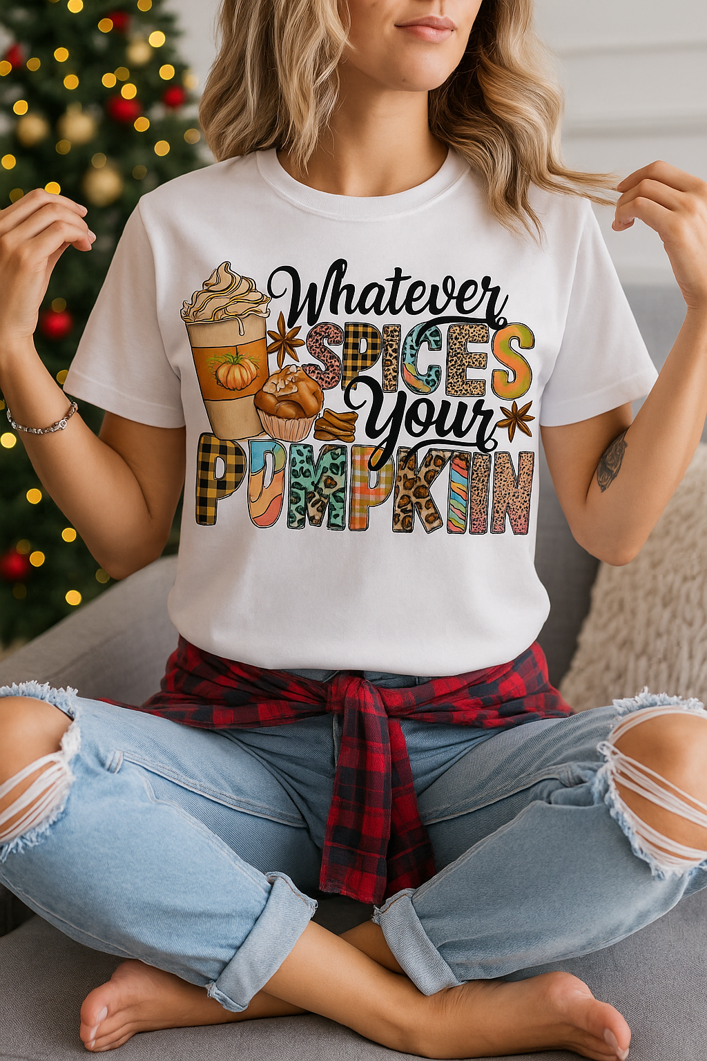 Woman wearing a white t-shirt that says “Whatever Spices Your Pumpkin” with colorful fall-themed lettering, pumpkin spice latte, muffin, and cinnamon stick graphics, seated casually in a cozy setting.